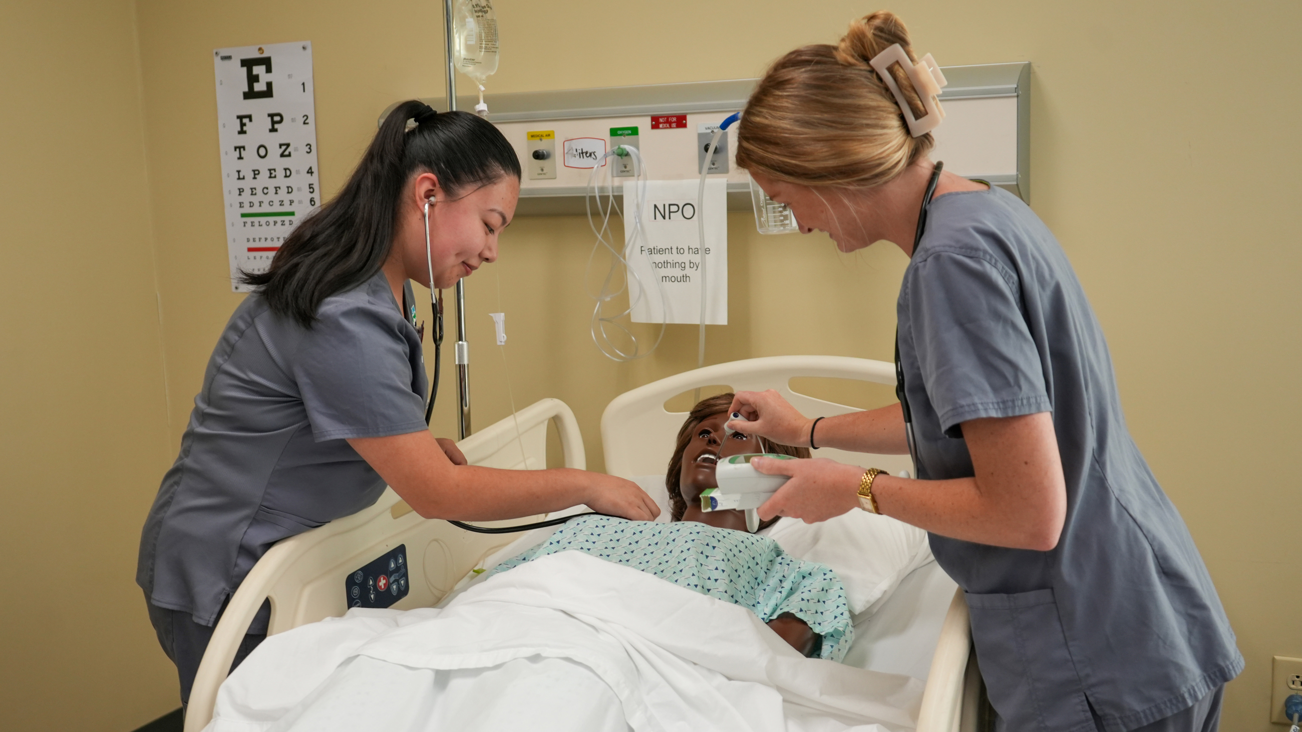 Two TCTC nursing students working over the bed of a fake patient checking their temperature and heart rate. 